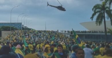 Pôster do filme No Céu da Pátria Nesse Instante, mostrando uma manifestação em Brasília com milhares de pessoas vestindo roupas amarelas e verdes, segurando bandeiras do Brasil, enquanto um helicóptero sobrevoa o local em frente a um prédio icônico. Imagem retirada do nosso blog Multi Nerdz.