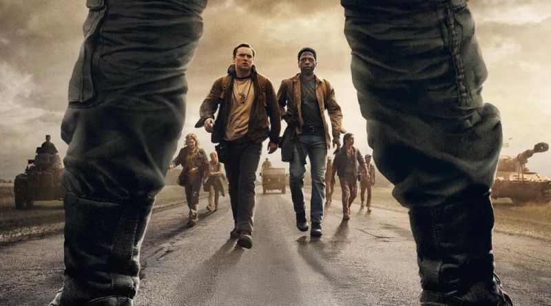 Pôster do filme A Longa Marcha, com um grupo de pessoas caminhando por uma estrada, em frente a soldados e tanques. A imagem é capturada a partir da perspectiva de dois soldados, com o foco nos pés e nas botas, enquanto o grupo se aproxima, criando uma atmosfera de tensão e conflito.