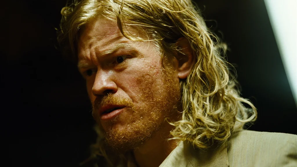 Jesse Plemons em cena do filme Bugonia com cabelos longos loiros e barba, em closeup de perfil com expressão séria em iluminação dourada e fundo escuro. Conteúdo do Multi Nerdz.
