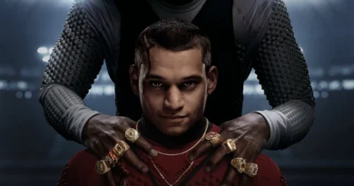 Imagem promocional do filme GOAT (Him) mostra um jovem com expressão séria vestindo uma roupa vermelha, enquanto uma figura maior, com mangas acolchoadas e oito anéis dourados de campeão, segura seus ombros em um ambiente escuro iluminado por luzes de estádio.