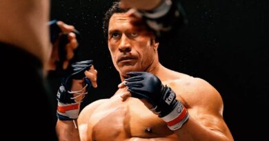 Dwayne “The Rock” Johnson aparece caracterizado como o lutador Mark Kerr em uma cena intensa do filme Coração de Lutador. Com luvas de MMA e expressão séria, ele está em posição de combate dentro do ringue, pronto para enfrentar o oponente. O suor e o sangue em seu rosto destacam a intensidade da luta, enquanto o fundo escuro realça o clima dramático do momento.