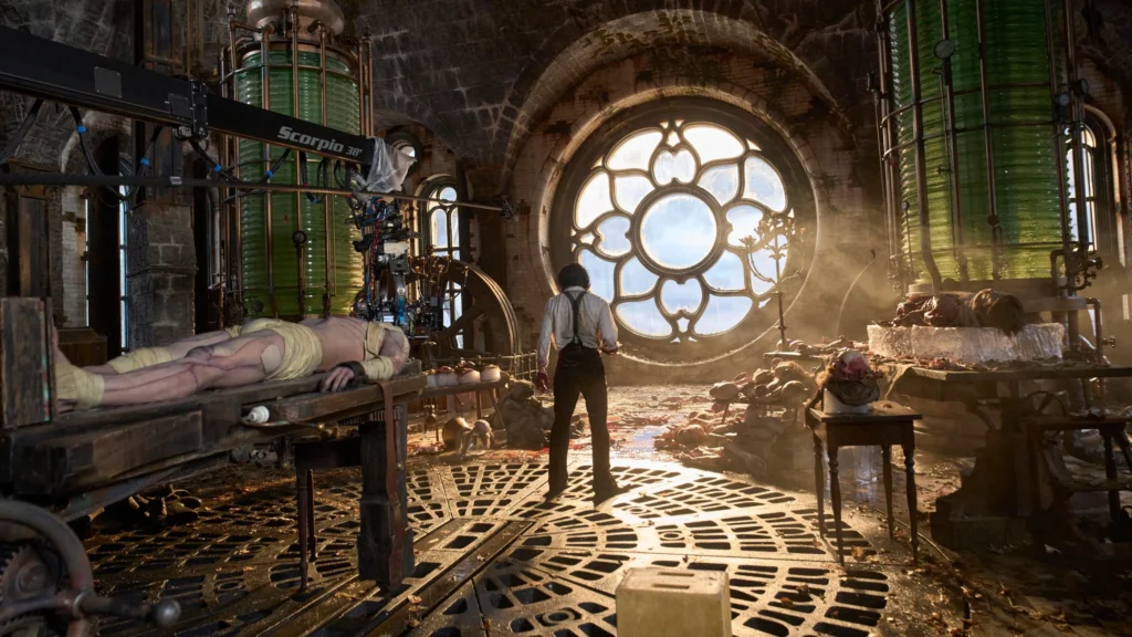 Visão ampla do laboratório de Victor Frankenstein no filme de Guillermo del Toro, com grandes tanques verdes, equipamentos científicos vintage e o corpo inerte da criatura sobre uma mesa, enquanto Victor observa o cenário iluminado pela luz que atravessa um enorme vitral circular.