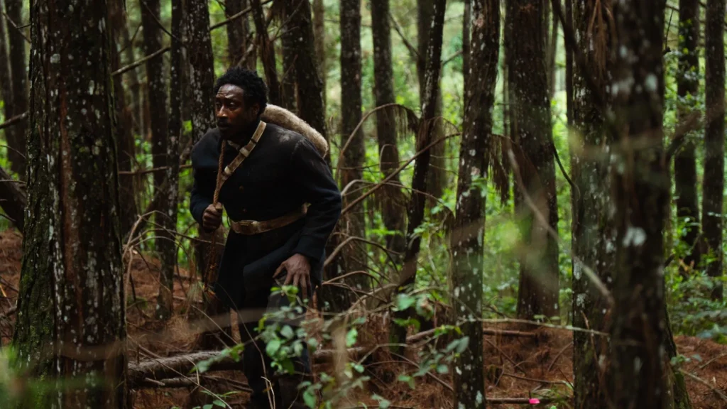Personagem vivido por Jorge Guerreiro atravessando floresta densa com saco nas costas em cena do filme 'A Própria Carne' do Jovem Nerd.