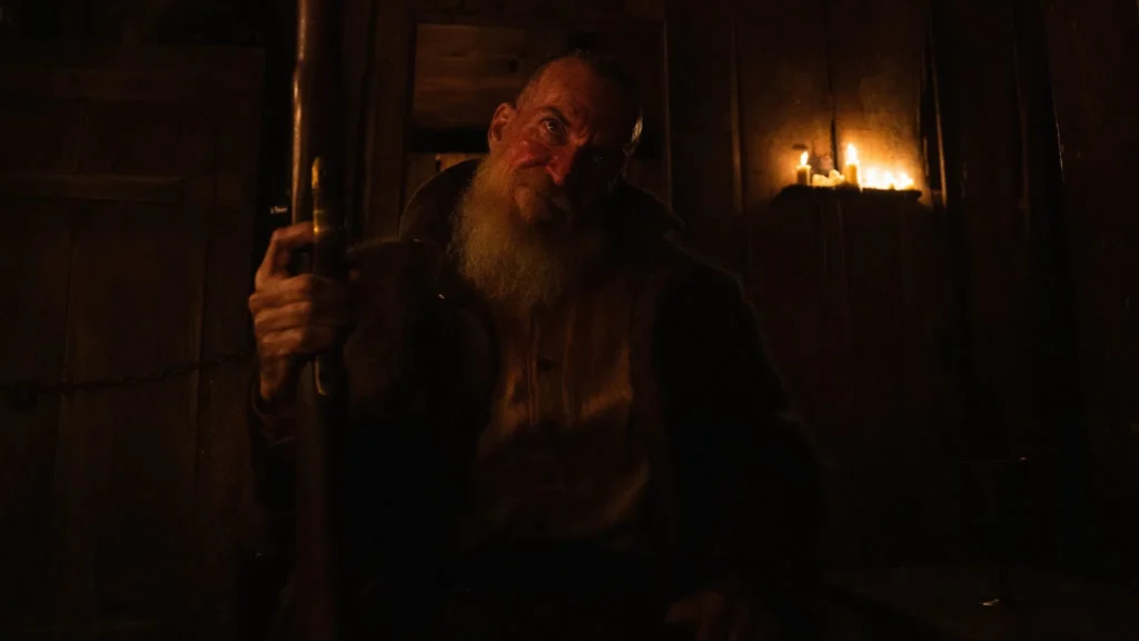 Luiz Carlos Persy segurando uma espingarda em cabana pouco iluminada por vela, cena do filme 'A Própria Carne' do Jovem Nerd.