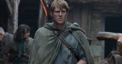 Peter Claffey como Sor Duncan em cena de O Cavaleiro dos Sete Reinos, vestindo uma capa rústica cinza esverdeada com uma alça de couro no peito, olhando para frente com expressão de preocupação em um vilarejo medieval.