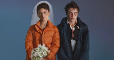 Um retrato de estúdio em plano médio de Zendaya e Robert Pattinson como seus personagens no filme O Drama. Zendaya, à esquerda, usa um vestido de noiva branco e véu, coberto por uma jaqueta puffer laranja brilhante, segurando um buquê de flores brancas com uma expressão séria e angustiada. Robert Pattinson, à direita, veste um terno preto desarrumado com camisa social branca manchada de sangue e gravata solta, coberto por uma jaqueta esportiva azul marinho. Seu rosto está visivelmente machucado, com hematomas e sangue. Ambos têm expressões melancólicas e olham para a frente. O fundo é um gradiente suave de azul para roxo-azulado. Capa da crítica do filme no blog Multi Nerdz.