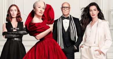Imagem promocional e capa do filme O Diabo Veste Prada 2, mostrando os quatro atores protagonistas posando lado a lado em estilo de editorial de moda, contra um fundo branco com molduras clássicas. Da esquerda para a direita: Emily Blunt com cabelos ruivos ondulados, vestindo um vestido preto estruturado com fivelas e luvas longas de couro preto, de braços cruzados; Meryl Streep com cabelos brancos, em destaque usando um exuberante e volumoso vestido vermelho com gola escultural; Stanley Tucci, careca e com óculos de aros grossos, usando smoking preto com colete, gravata borboleta de bolinhas e um cachecol listrado em preto e branco; e Anne Hathaway com longos cabelos escuros esvoaçantes, vestindo um elegante conjunto de alfaiataria branco de cetim adornado com um cinto de correntes e pérolas com a logo da Chanel. Todos exibem feições sérias, sofisticadas e imponentes. Capa da crítica do filme no blog Multi Nerdz.