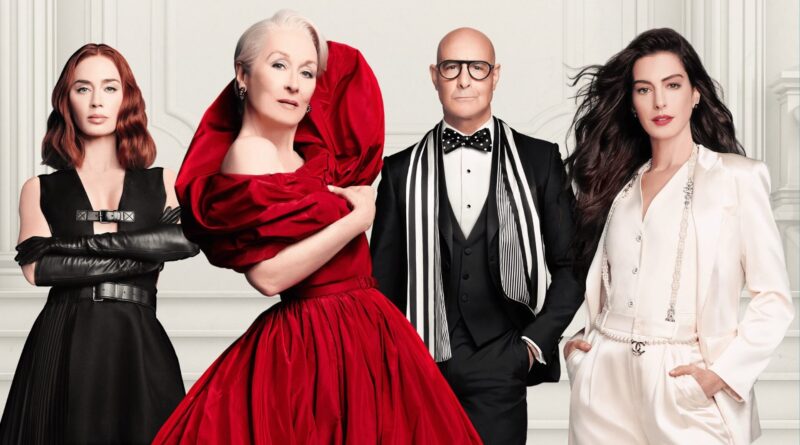 Imagem promocional e capa do filme O Diabo Veste Prada 2, mostrando os quatro atores protagonistas posando lado a lado em estilo de editorial de moda, contra um fundo branco com molduras clássicas. Da esquerda para a direita: Emily Blunt com cabelos ruivos ondulados, vestindo um vestido preto estruturado com fivelas e luvas longas de couro preto, de braços cruzados; Meryl Streep com cabelos brancos, em destaque usando um exuberante e volumoso vestido vermelho com gola escultural; Stanley Tucci, careca e com óculos de aros grossos, usando smoking preto com colete, gravata borboleta de bolinhas e um cachecol listrado em preto e branco; e Anne Hathaway com longos cabelos escuros esvoaçantes, vestindo um elegante conjunto de alfaiataria branco de cetim adornado com um cinto de correntes e pérolas com a logo da Chanel. Todos exibem feições sérias, sofisticadas e imponentes. Capa da crítica do filme no blog Multi Nerdz.