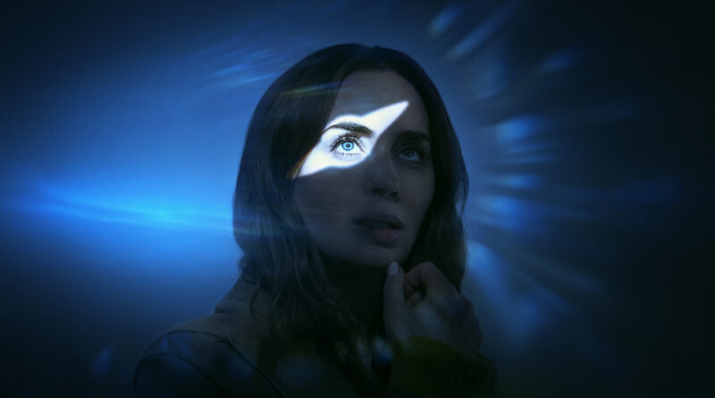 Emily Blunt em cena de Dia D, filme dirigido por Steven Spielberg, com iluminação azul e feixe de luz destacando seu olhar em meio a um ambiente escuro e enigmático. A atriz demonstra expressão séria e reflexiva em uma das cenas do longa. Imagem de destaque da crítica do filme no Multi Nerdz.
