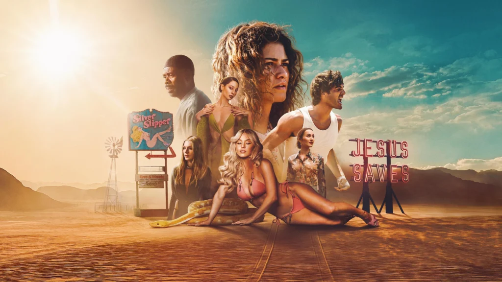 Pôster promocional da 3ª temporada da série Euphoria, com os personagens principais em uma montagem sobre uma paisagem de deserto árido sob um sol forte e brilhante. No centro superior, o rosto de Zendaya (Rue) ganha destaque; ela tem os cabelos cacheados bagunçados e uma expressão angustiada. Em primeiro plano, no chão de areia, Sydney Sweeney (Cassie) posa deitada sensualmente usando um biquíni rosa, com uma grande cobra píton amarela e branca enrolada próxima a ela. À esquerda, aparecem Colman Domingo (Ali) de perfil, Alexa Demie (Maddy) em um vestido verde decotado e Hunter Schafer (Jules) com feição séria. À direita, Jacob Elordi (Nate) veste uma regata branca e grita furiosamente, enquanto Maude Apatow (Lexi) está abaixo dele com uma camisa estampada. O cenário surreal inclui uma placa vintage de motel chamada "Silver Slipper", um moinho de vento, e uma estrutura com um letreiro em neon vermelho que diz "JESUS SAVES" (Jesus Salva). Marcas de pneus cruzam a areia em direção ao espectador. Capa da crítica da série no blog Multi Nerdz.