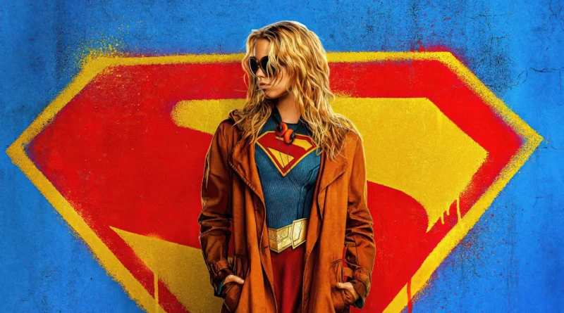 Imagem promocional da atriz Milly Alcock caracterizada como a protagonista do filme Supergirl. Ela está no centro da imagem em uma pose descolada, com as mãos nos bolsos de um sobretudo marrom que está aberto, revelando por baixo o clássico traje azul texturizado da heroína, com o escudo do 'S' em vermelho e amarelo no peito, cinto dourado e saia vermelha. Ela tem cabelos loiros ondulados, olha para a esquerda e usa óculos escuros, além de fones de ouvido laranjas ao redor do pescoço. O fundo é uma parede azul brilhante e texturizada com um enorme escudo do 'S' em vermelho e amarelo pintado em estilo grafite, com bordas esfumaçadas e respingos de tinta. Capa da crítica do filme Supergirl no canal Multi Nerdz.