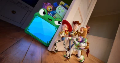 Cena da animação Toy Story 5 em um quarto com chão de madeira. À direita, os brinquedos clássicos Jessie, Buzz Lightyear, Woody e o cavalo Bala no Alvo estão encolhidos e escondidos atrás do batente de uma porta branca. Eles espiam o outro cômodo com expressões de medo, choque e apreensão. À esquerda, iluminados pelo forte brilho azul de uma tela, estão um grupo de brinquedos eletrônicos modernos, com grande destaque para um tablet envolto em uma capa protetora verde em formato de sapo com olhos grandes. Atrás do tablet, empilham-se outros gadgets tecnológicos, incluindo uma câmera digital roxa e um dispositivo inteligente com tela sorridente. Capa da crítica do filme Toy Story 5 no blog Multi Nerdz.