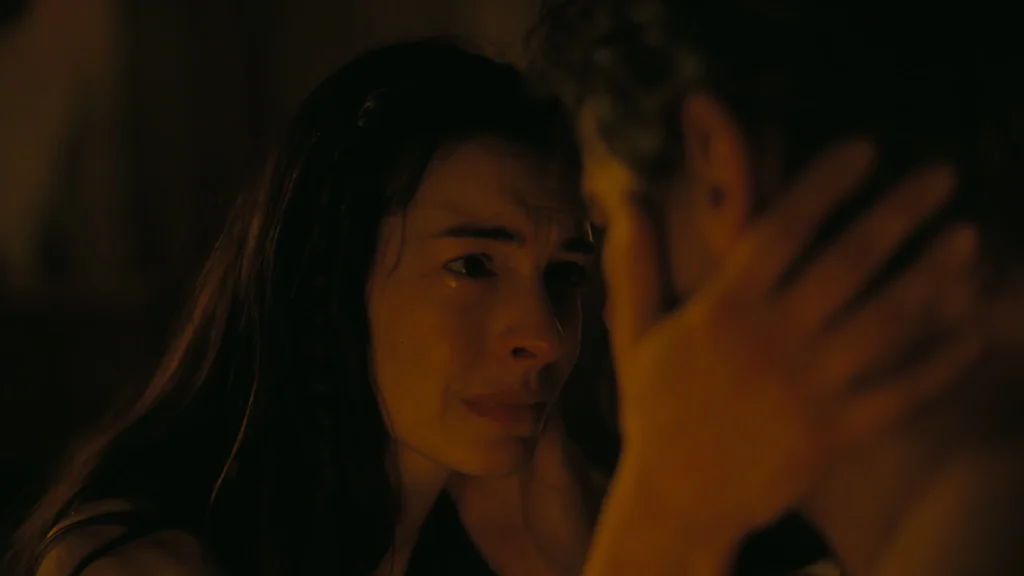 Anne Hathaway aparece em destaque, emocionada e com os olhos marejados, tocando o rosto de Matt Damon em uma cena iluminada por tons quentes do filme ‘A Odisseia’.