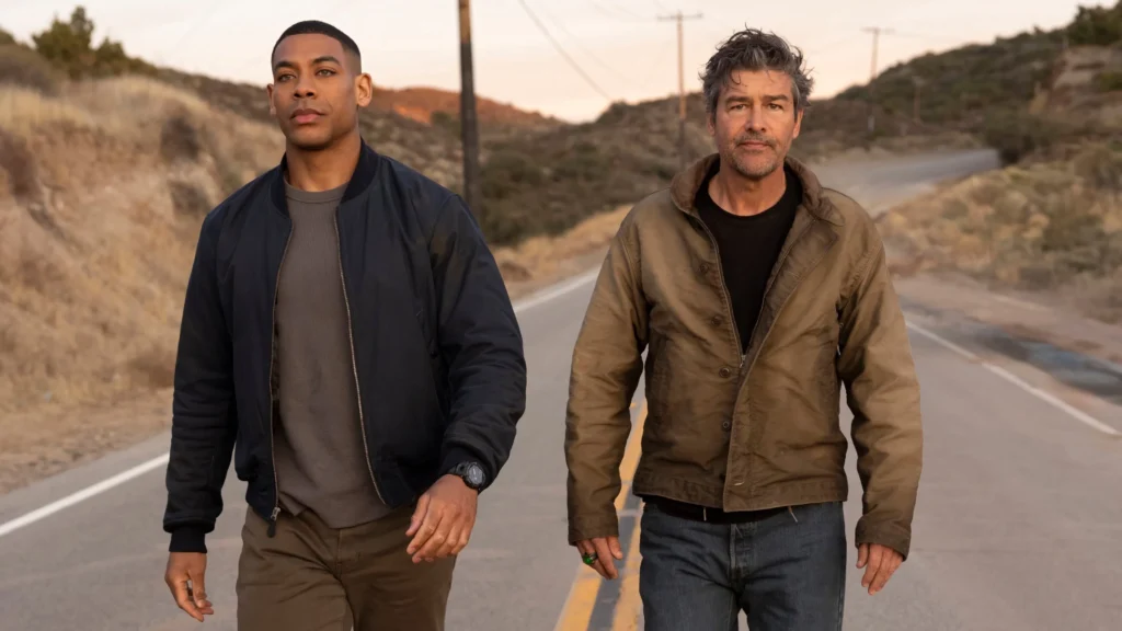 Aaron Pierre como John Stewart e Kyle Chandler como Hal Jordan caminham lado a lado por uma estrada em meio a uma paisagem árida ao entardecer, em imagem promocional da série ‘Lanternas’.