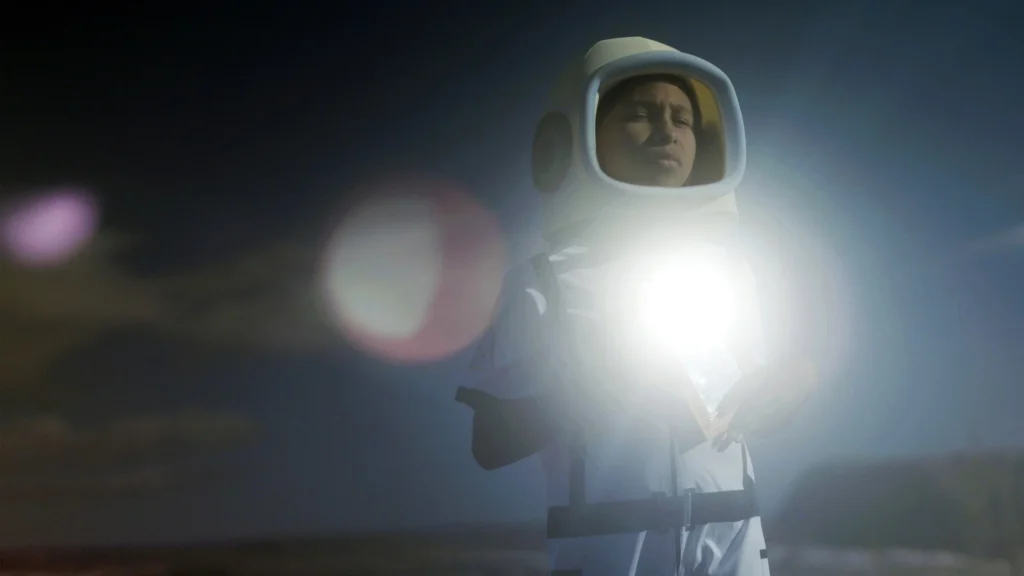 Uma das jovens protagonistas de ‘A Fabulosa Máquina do Tempo’ aparece usando um traje que lembra uma roupa de astronauta, iluminada por uma forte luz frontal, em cena do documentário de Eliza Capai sobre meninas do sertão do Piauí e seus sonhos de futuro.