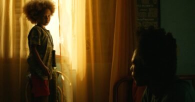 Efraim Santos como Tutu aparece em pé diante de uma janela iluminada por uma forte luz dourada, enquanto Flip como Guto surge sentado em primeiro plano, parcialmente em sombra, em uma cena de ‘Nosso Segredo’. O contraste entre a luz quente e o ambiente escuro reforça o clima íntimo e dramático da sequência.